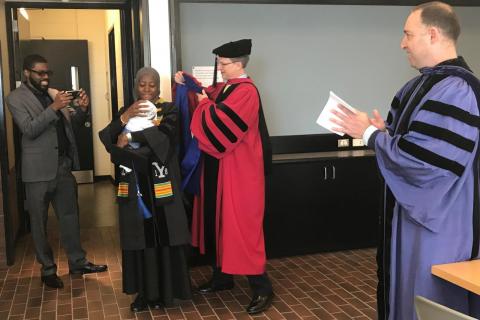 Craig Crews hooding Jemilat Salami (with her son). (Photo by Denise George)